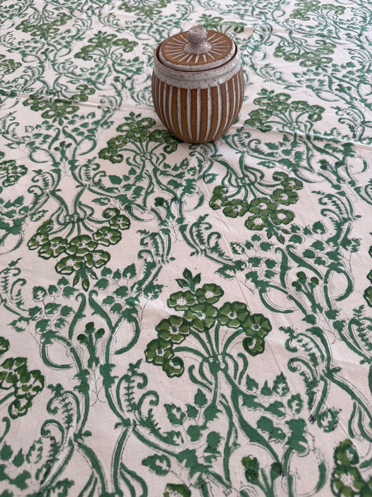 House of Mulmul - Cotton Table Cloth Round. Close-up of a decorative green and white fabric with a floral pattern and a wooden knob.