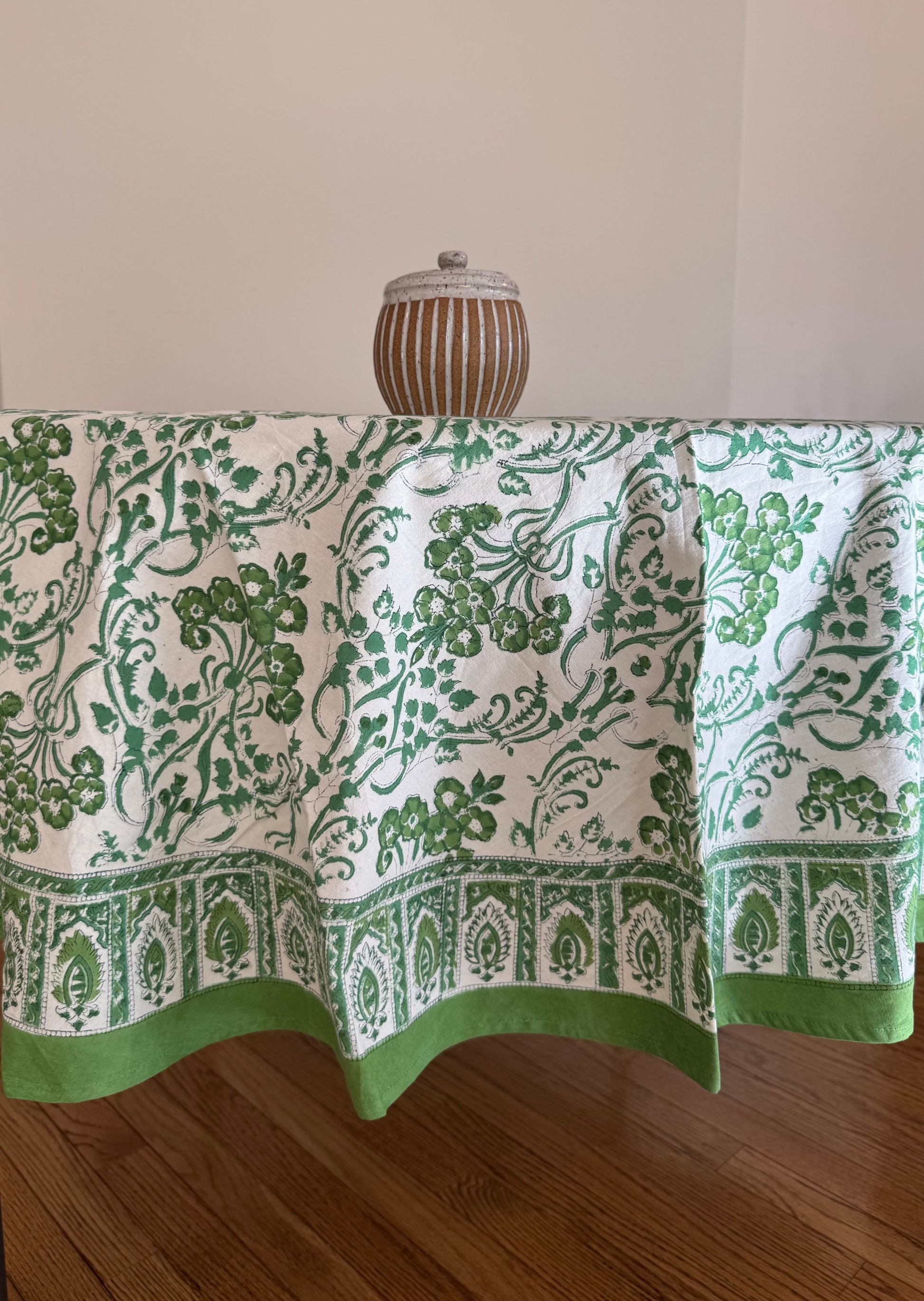 House of Mulmul - Cotton Table Cloth Round. Green and white patterned tablecloth on a wooden table with a neutral background