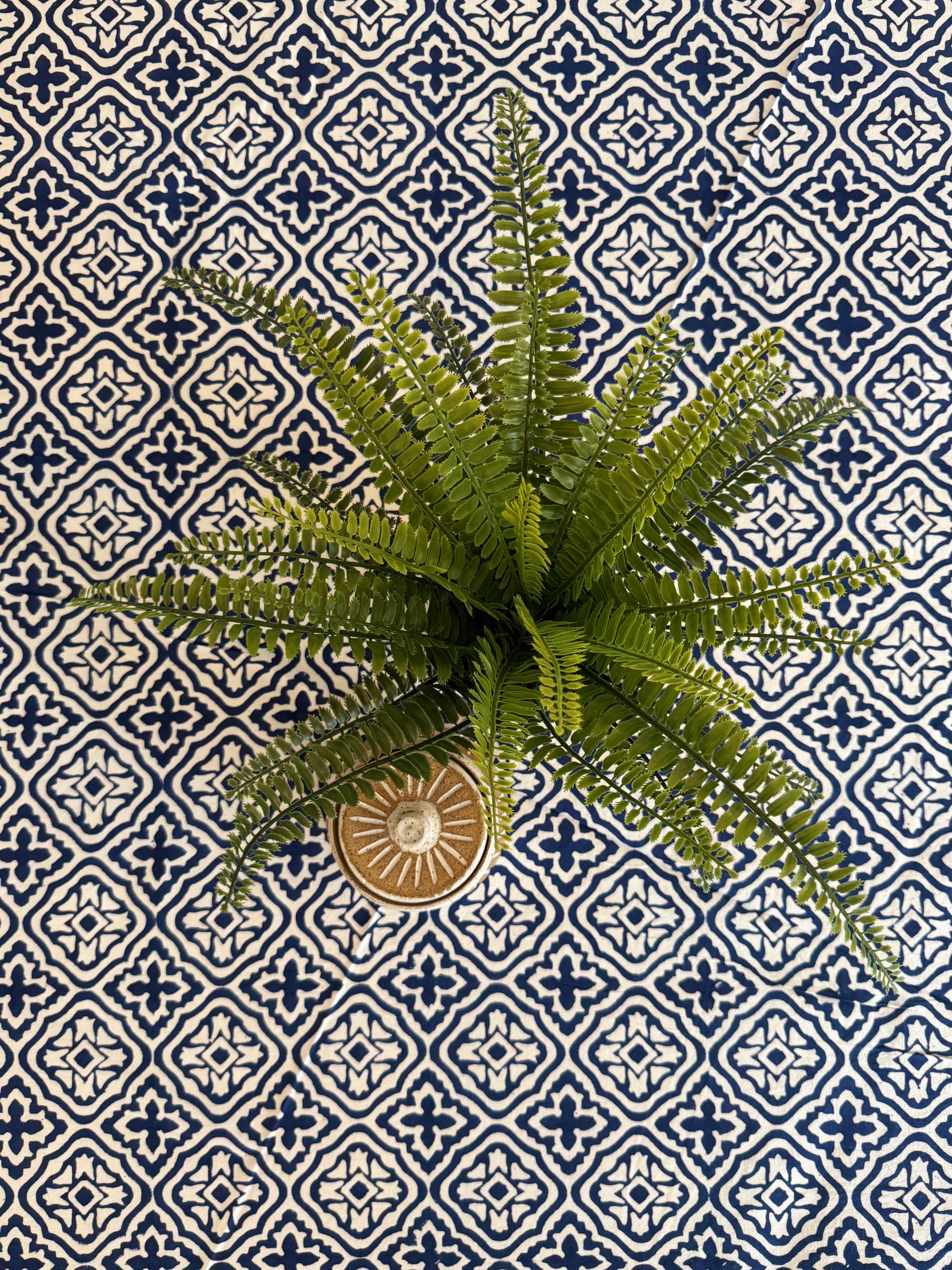 House of Mulmul - Cotton Table Cloth Round. Artificial fern plant in a decorative pot on a blue and white patterned tile background