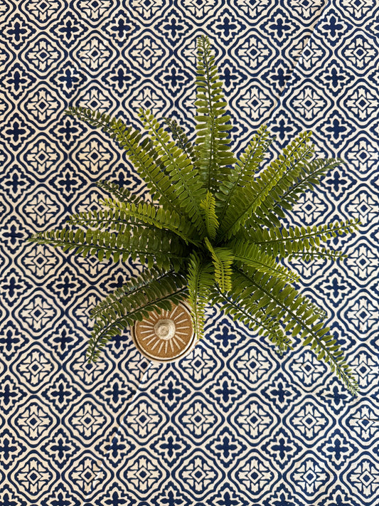 House of Mulmul - Cotton Table Cloth Round. Artificial fern plant in a decorative pot on a blue and white patterned tile background