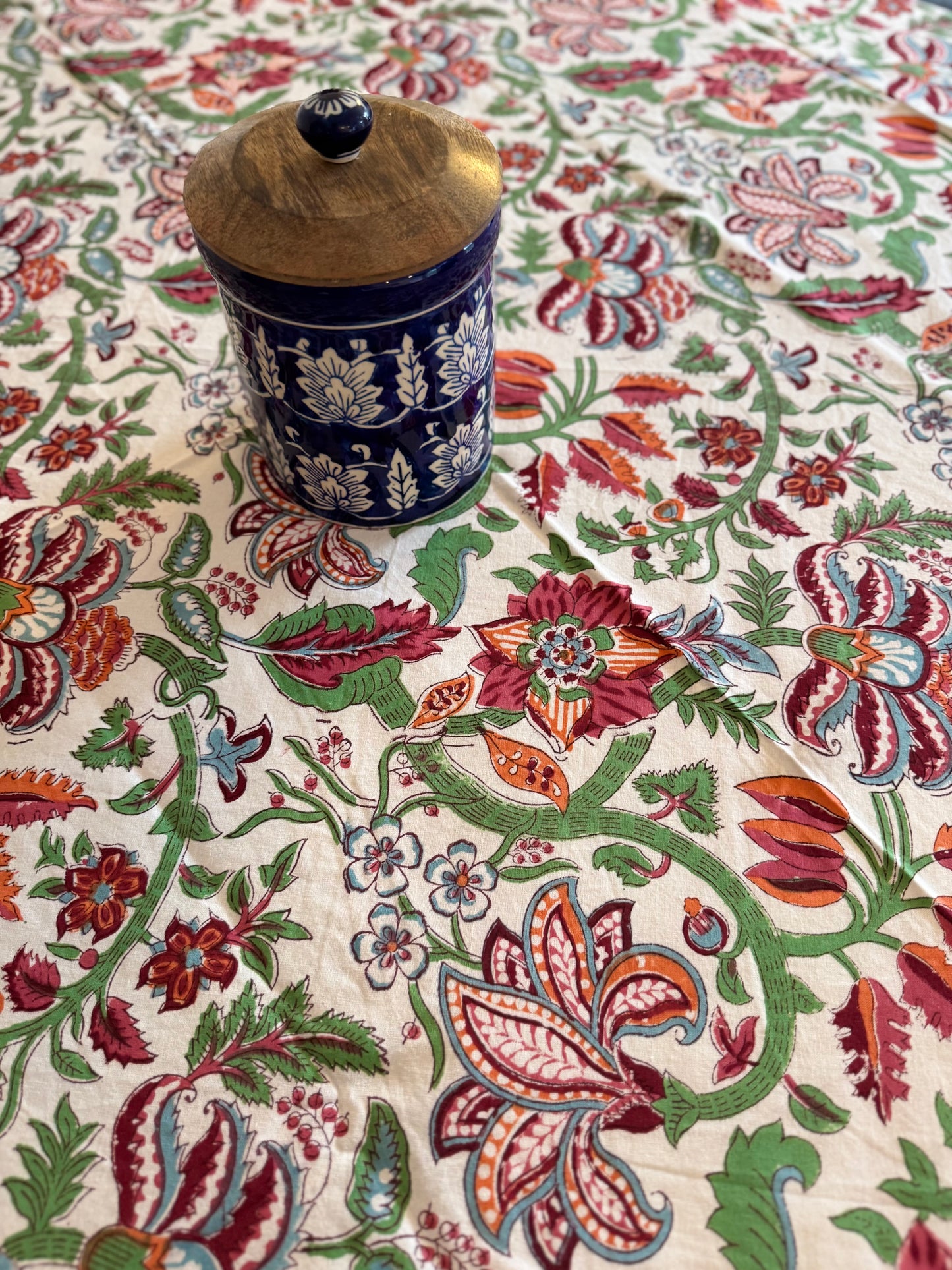 House of Mulmul - Cotton Table Cloth Round. Decorative fabric with intricate floral patterns and a ceramic jar on top.