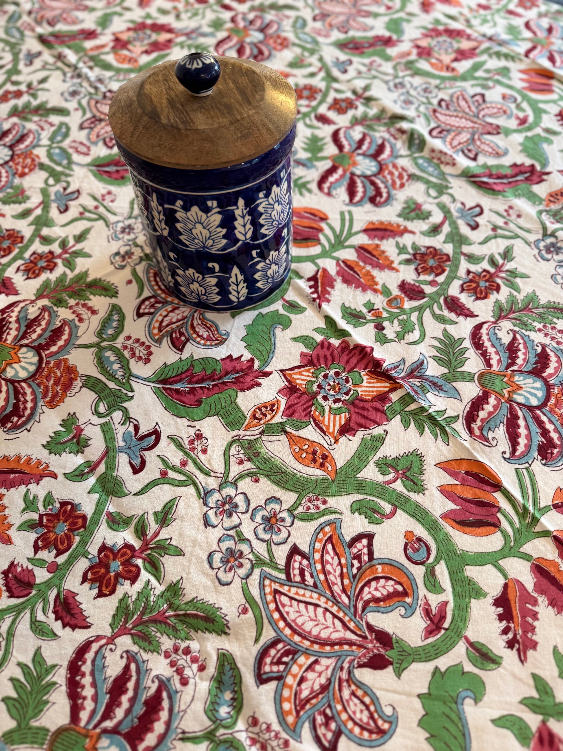 House of Mulmul - Cotton Table Cloth Round. Decorative fabric with intricate floral patterns and a ceramic jar on top.