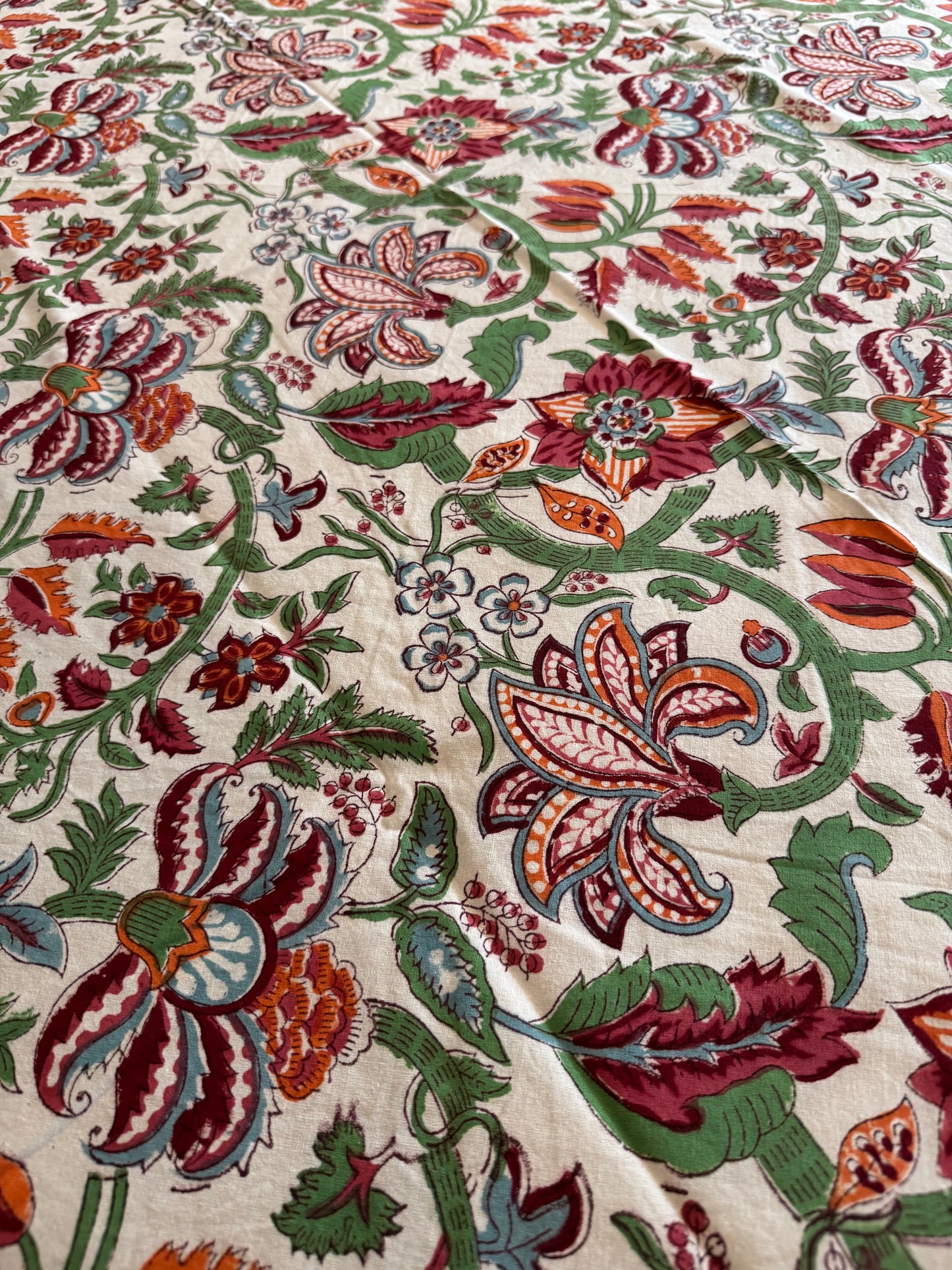 House of Mulmul - Cotton Table Cloth Round. Close-up of a fabric with intricate floral and paisley patterns in red, green, and brown on a beige background.