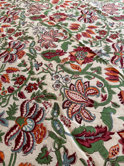 House of Mulmul - Cotton Table Cloth Round. Close-up of a fabric with intricate floral and paisley patterns in red, green, and brown on a beige background.