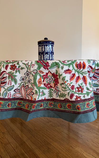 House of Mulmul - Cotton Table Cloth Round. Floral-patterned tablecloth on a wooden table with a decorative vase.
