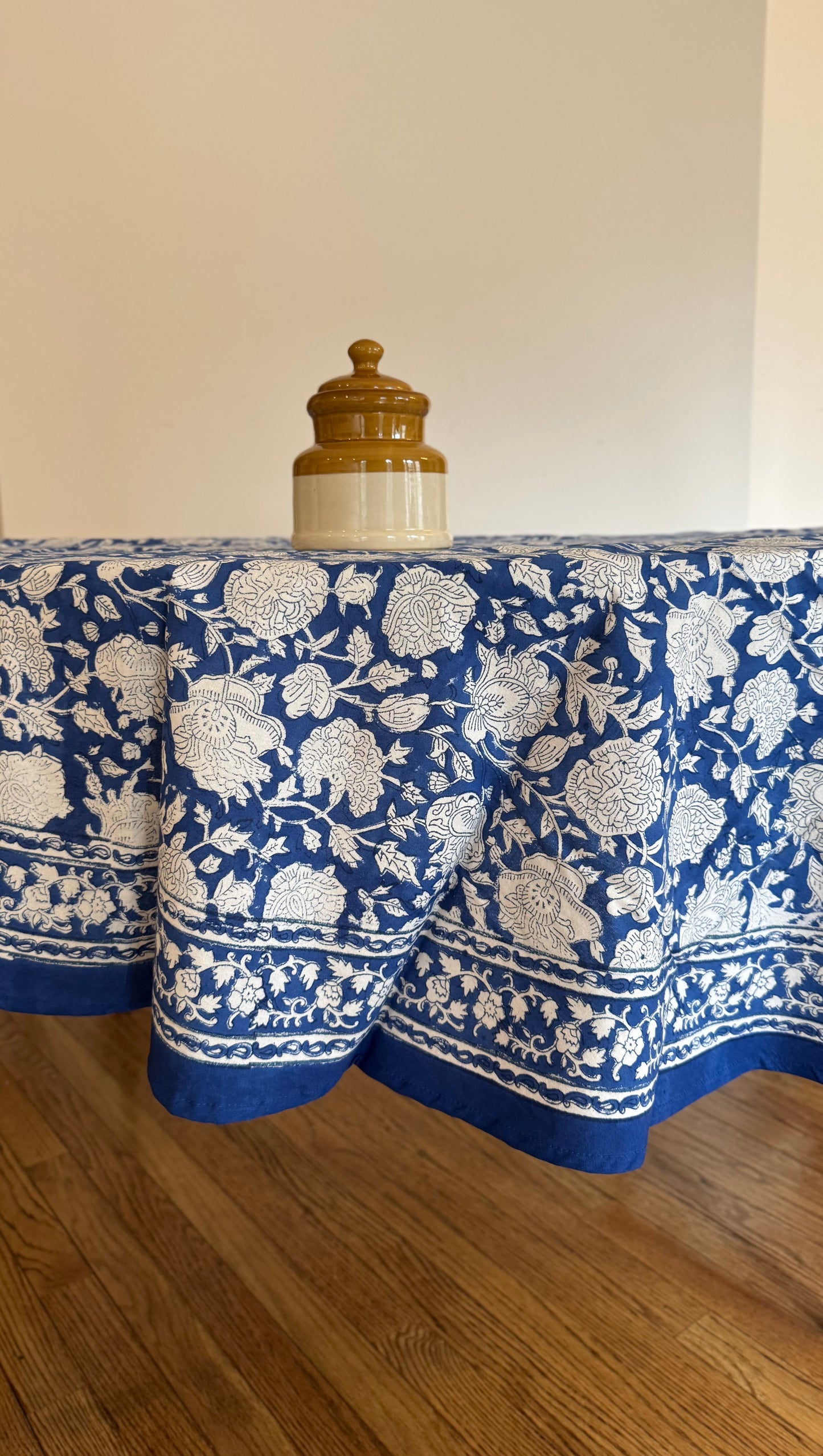 House of Mulmul - Cotton Table Cloth Round. Blue and white patterned tablecloth on a wooden table with a plain background