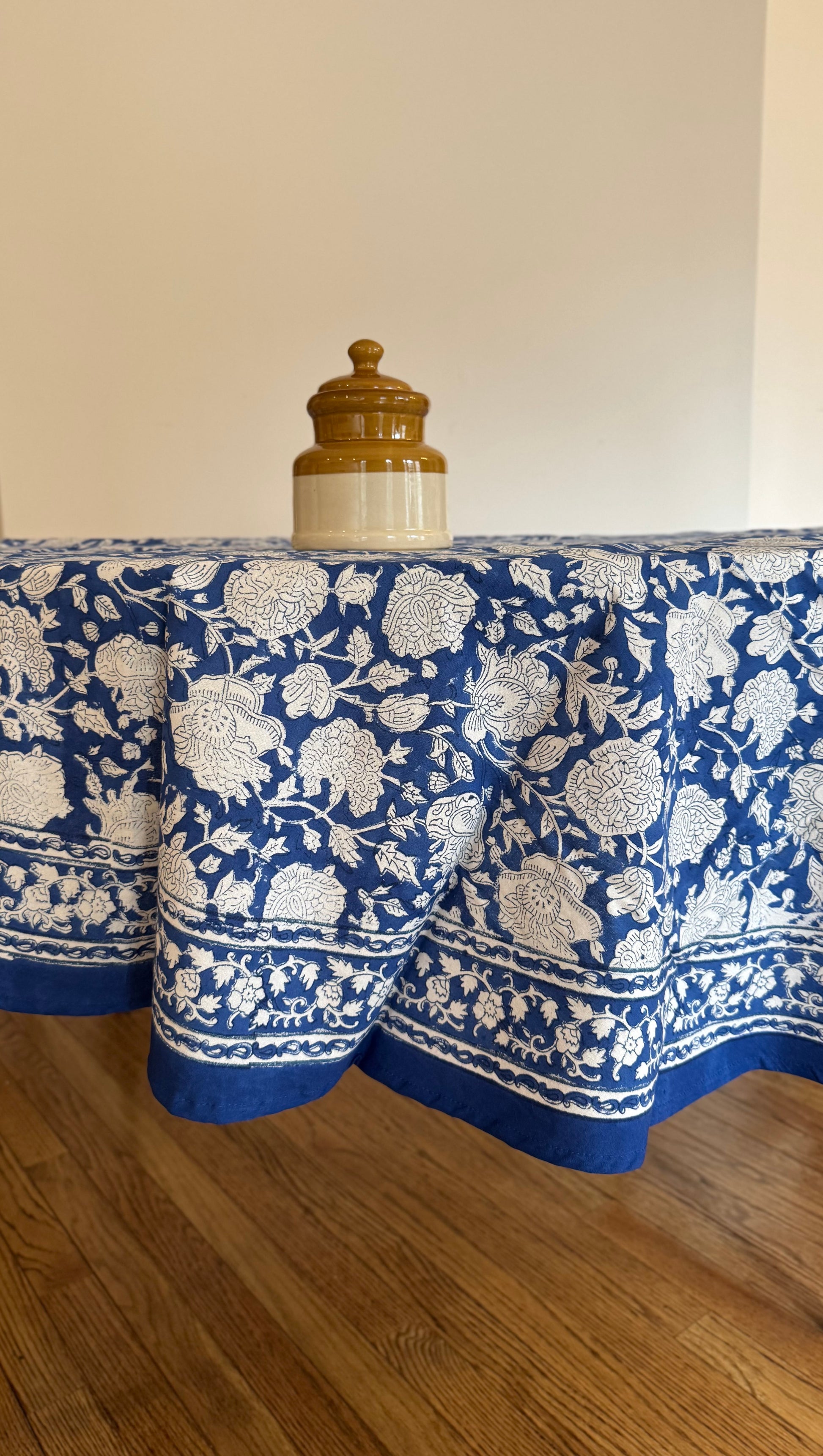 House of Mulmul - Cotton Table Cloth Round. Blue and white patterned tablecloth on a wooden table with a plain background