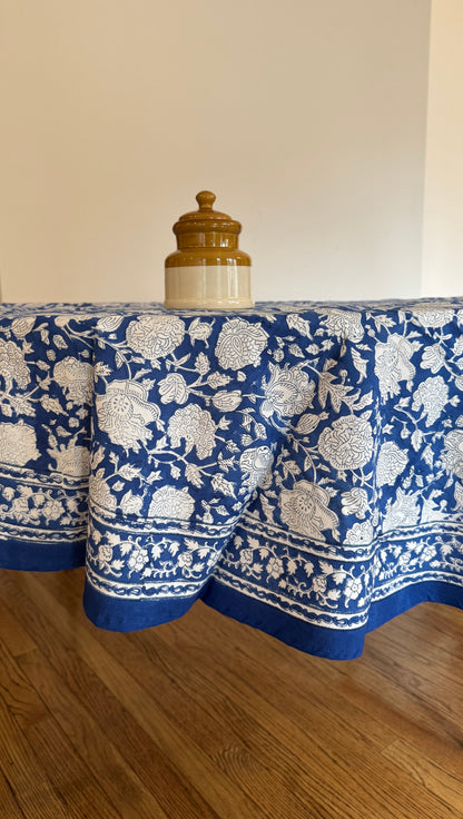 House of Mulmul - Cotton Table Cloth Round. Blue and white patterned tablecloth on a wooden table with a plain background