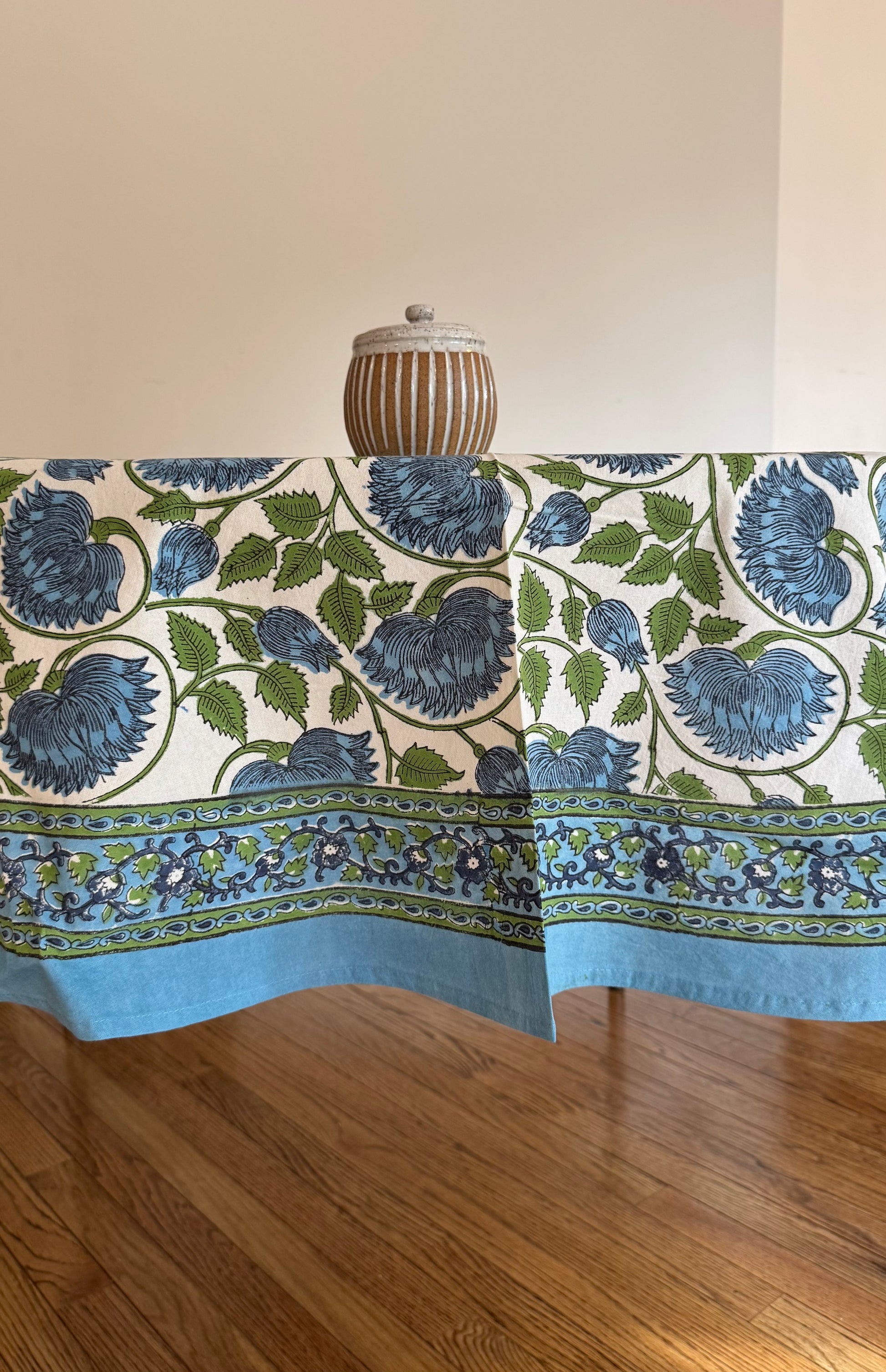 House of Mulmul - Cotton Table Cloth Round with green leaves, blue flower and white background pattern.
