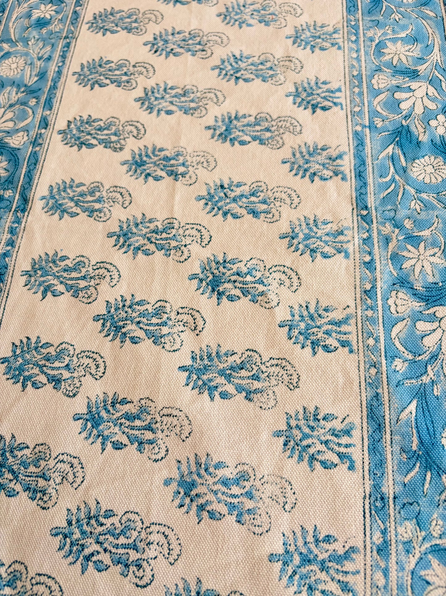 House of Mulmul - Cotton Blockprinted Table Runner. Close-up of a patterned table runner with blue and white designs on a beige background
