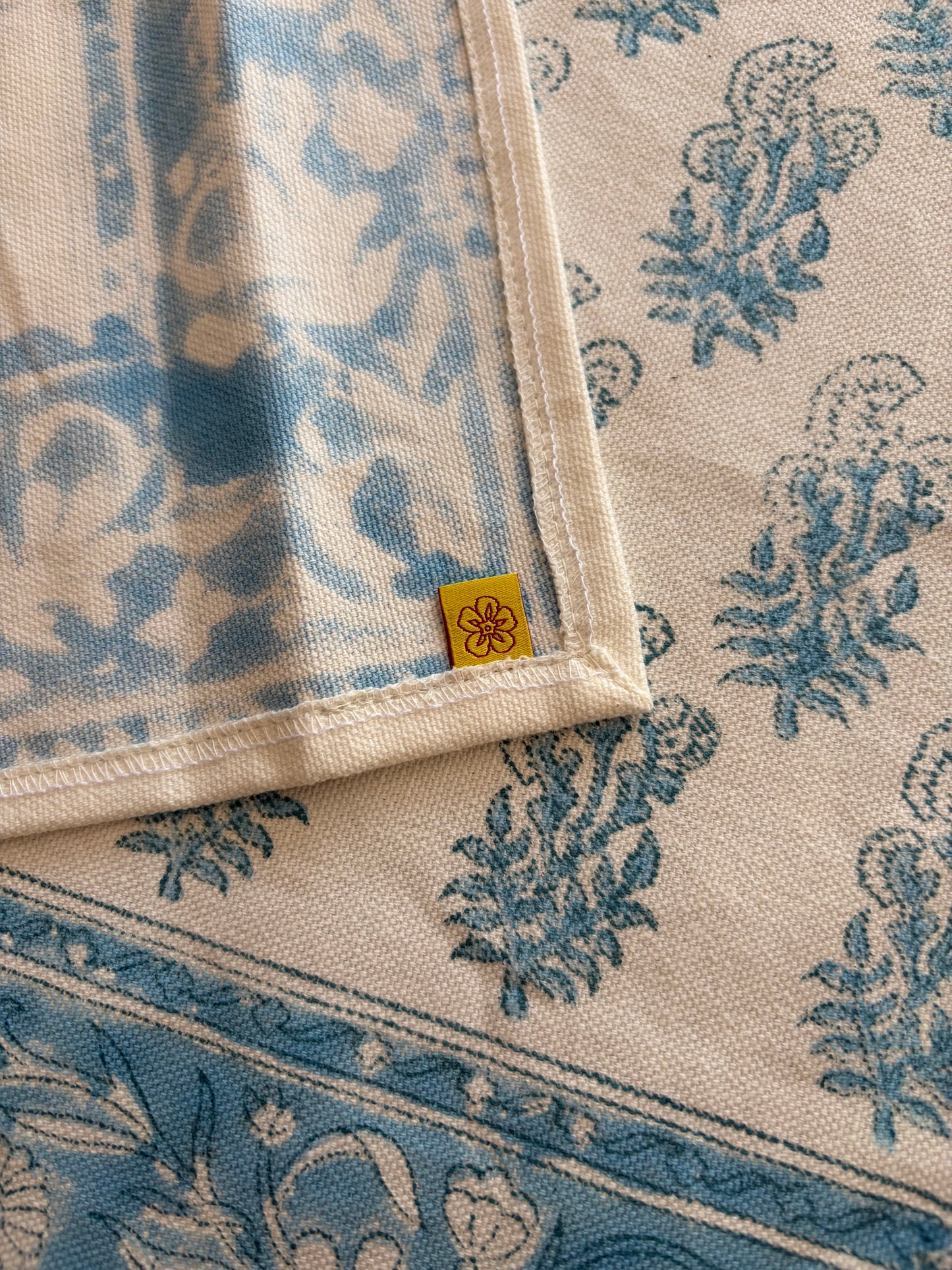 House of Mulmul - Cotton Blockprinted Table Runner. Close-up of a folded cotton runner with blue floral patterns on a beige background