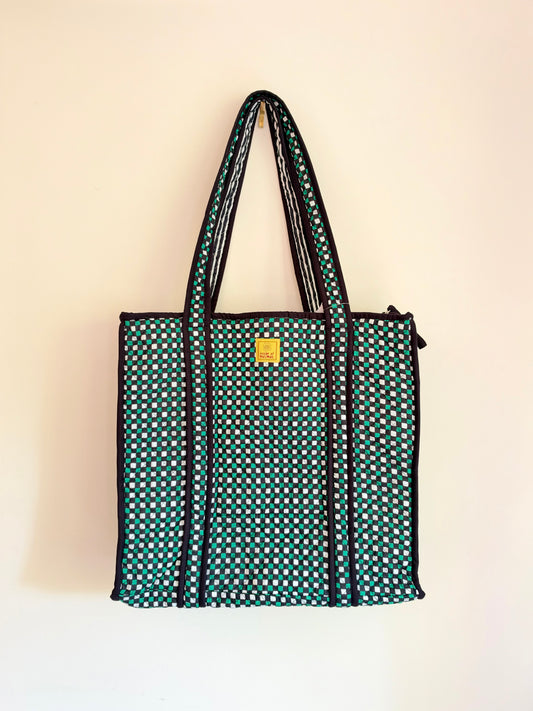 House of Mulmul - Cotton Tote Bags. A green tote bag with a white polka dot pattern, black trim, and two shoulder straps, hanging against a plain off-white wall.