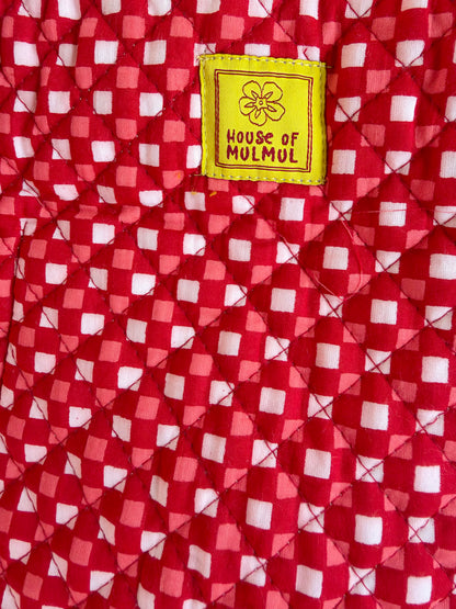 House of Mulmul - Cotton Tote Bags. Close-up of a red and white checkered quilted fabric with a yellow sewn-in label reading 'HOUSE OF MULMUL'.