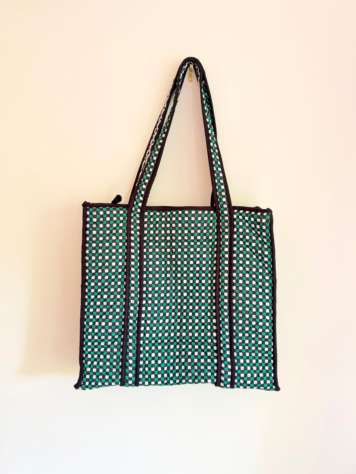 House of Mulmul - Cotton Tote Bags. A fabric tote bag with a green and white polka dot pattern and black trim, hanging against a plain off-white wall.