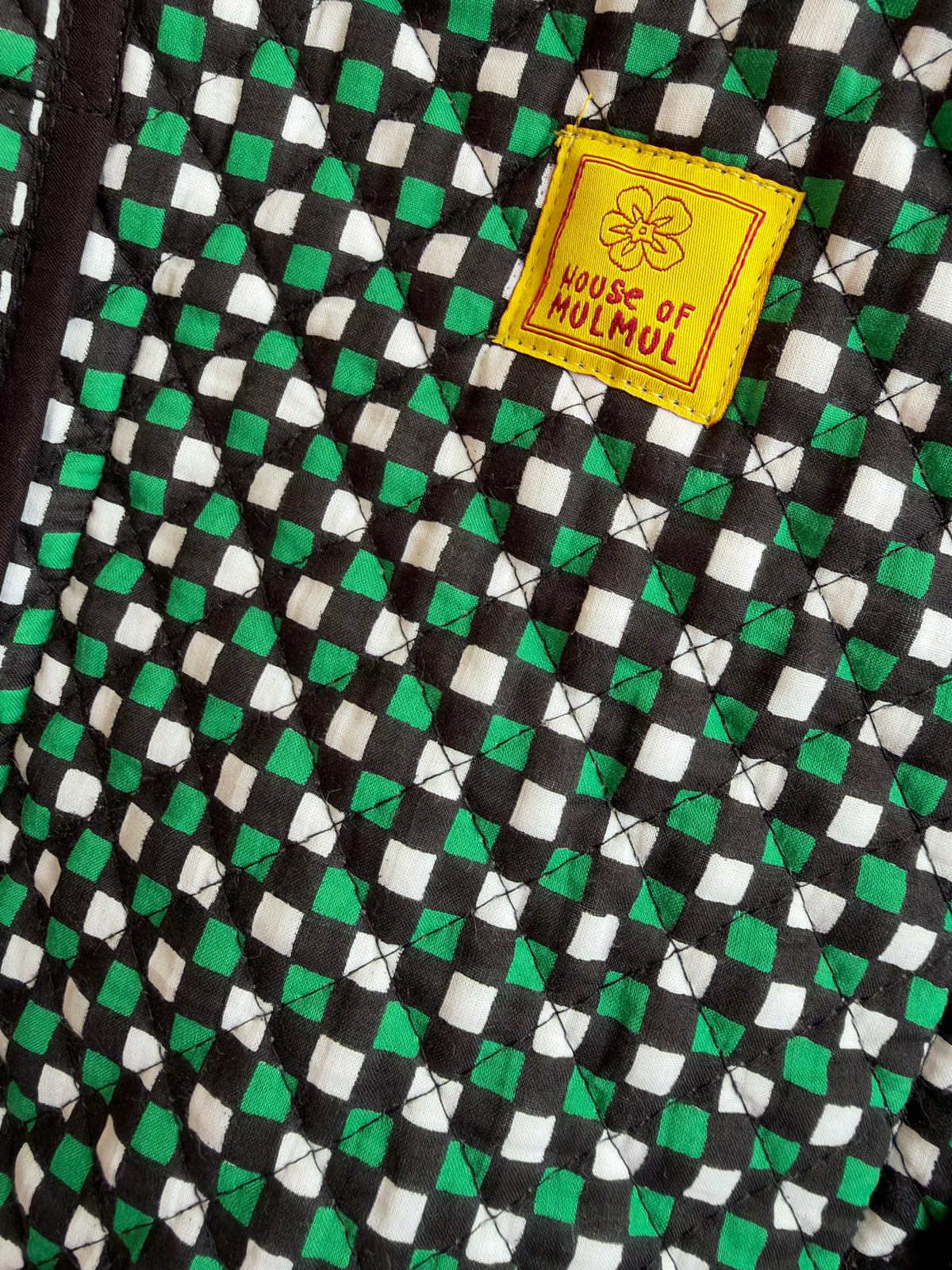 House of Mulmul - Cotton Tote Bags. Close-up of a quilted textile with a black, white, and green diamond pattern and a yellow sewn label reading 'HOUSE OF MULMUL'.