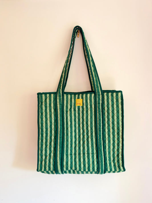 House of Mulmul - Cotton Tote Bags. A green and white striped canvas tote bag with dark green handles, hanging against a plain off-white wall.