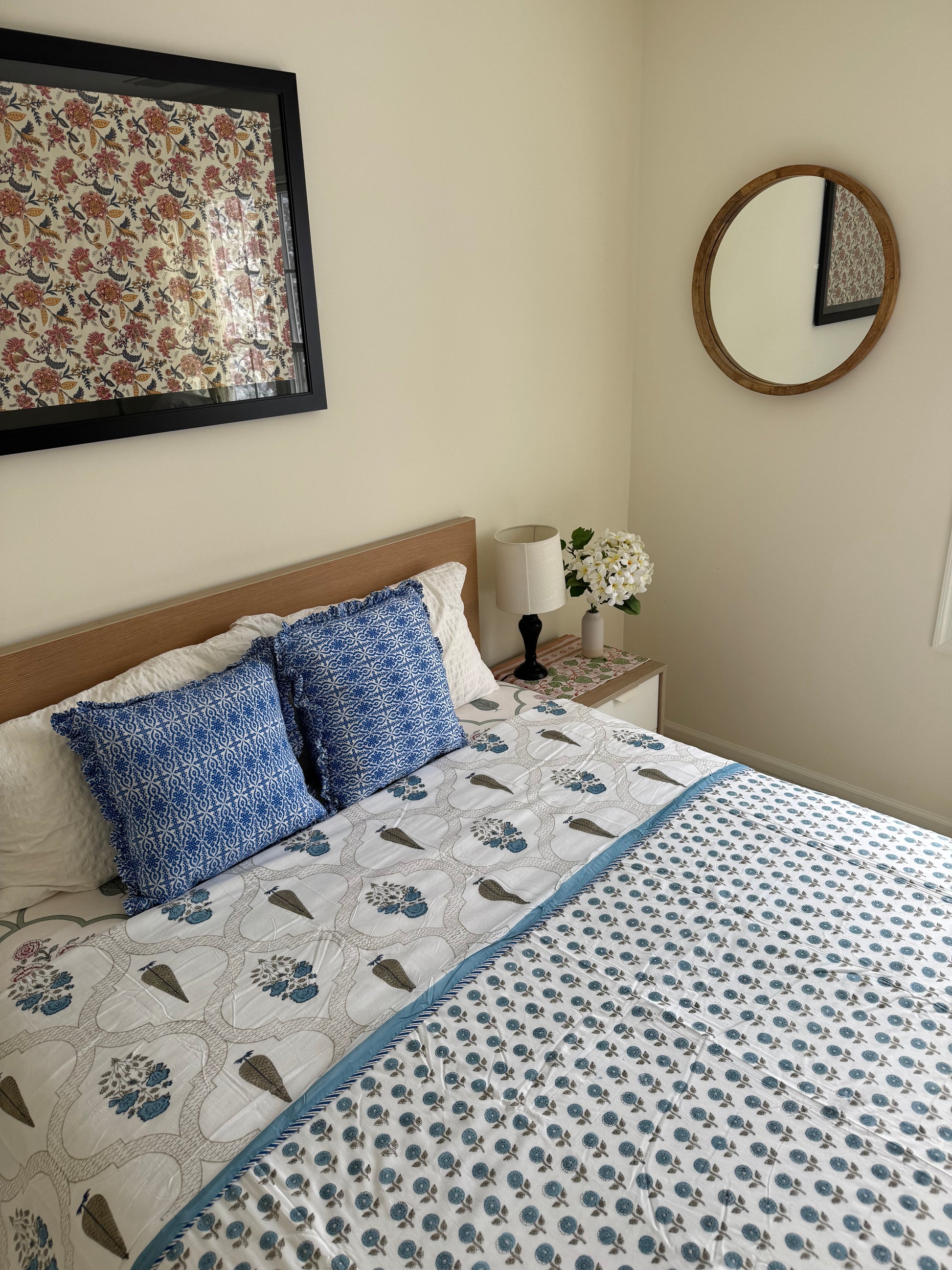 House of Mulmul - Coverlet Dohar blanket. Bedroom with reversible cotton coverlet blanket. Muslin dohar with palms cypress leaf and blue and brown colors, white background. Bedroom with floral curtains, mirror.