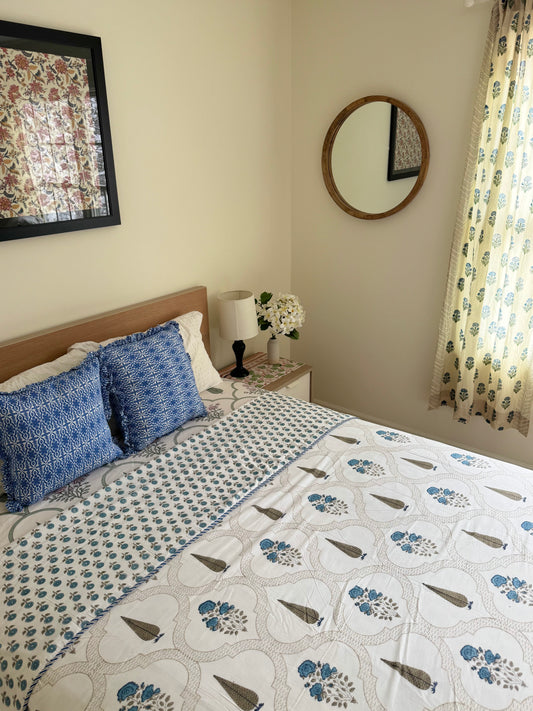 House of Mulmul - Coverlet Dohar blanket. Bedroom with reversible cotton coverlet blanket. Muslin dohar with palms cypress leaf and blue and brown colors, white background. With decorative elements floral curtains, mirror.