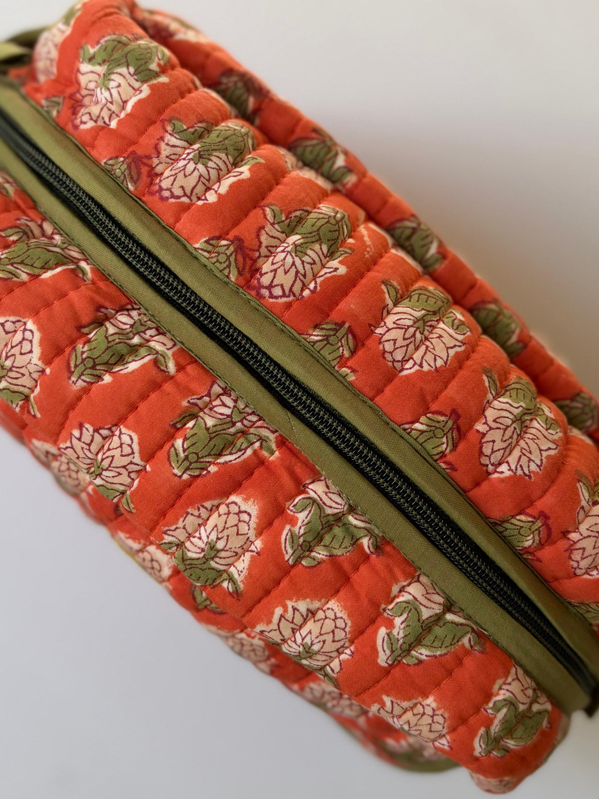 House of Mulmul - Handblock Printed Travel Makeup Quilted Pouch setA close-up of a quilted fabric zippered pouch in a vibrant orange-red color, decorated with a vintage-style floral print in pink and olive green, featuring a black zipper.