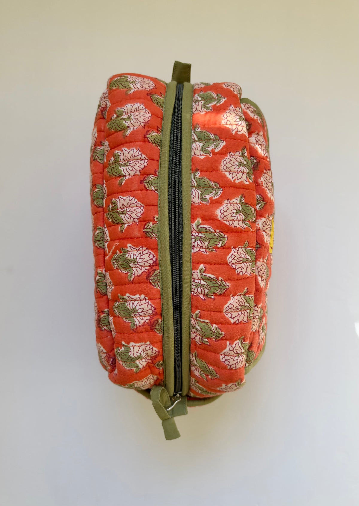 House of Mulmul - Handblock Printed Travel Makeup Quilted Pouch setA quilted cosmetic pouch with a vibrant orange-red background and a green, white, and pink floral pattern, featuring a green zipper.