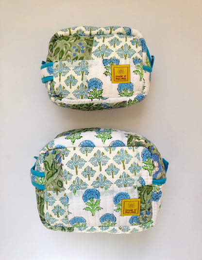 House of Mulmul - Handblock Printed Travel Makeup Quilted Pouch set. Two quilted pouches with a blue and green floral print on a white background, displayed vertically against a plain light wall. Each pouch has a small yellow brand patch that reads 'Paisley of Perth'.