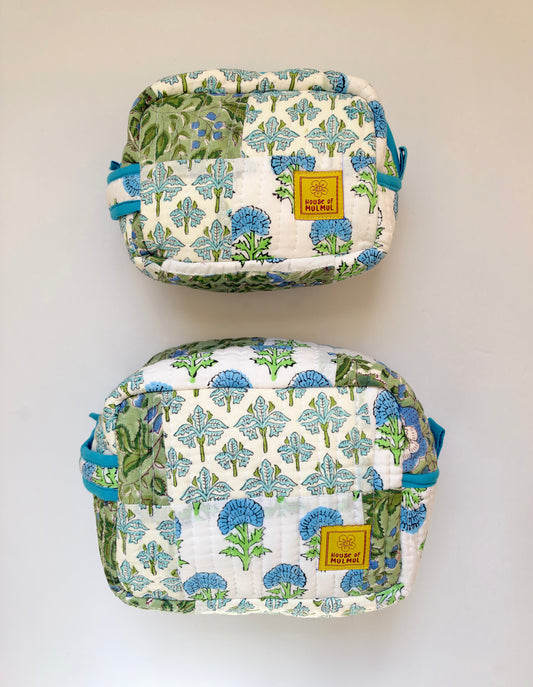 House of Mulmul - Handblock Printed Travel Makeup Quilted Pouch set. Two quilted pouches with a blue and green floral print on a white background, displayed vertically against a plain light wall. Each pouch has a small yellow brand patch that reads 'Paisley of Perth'.