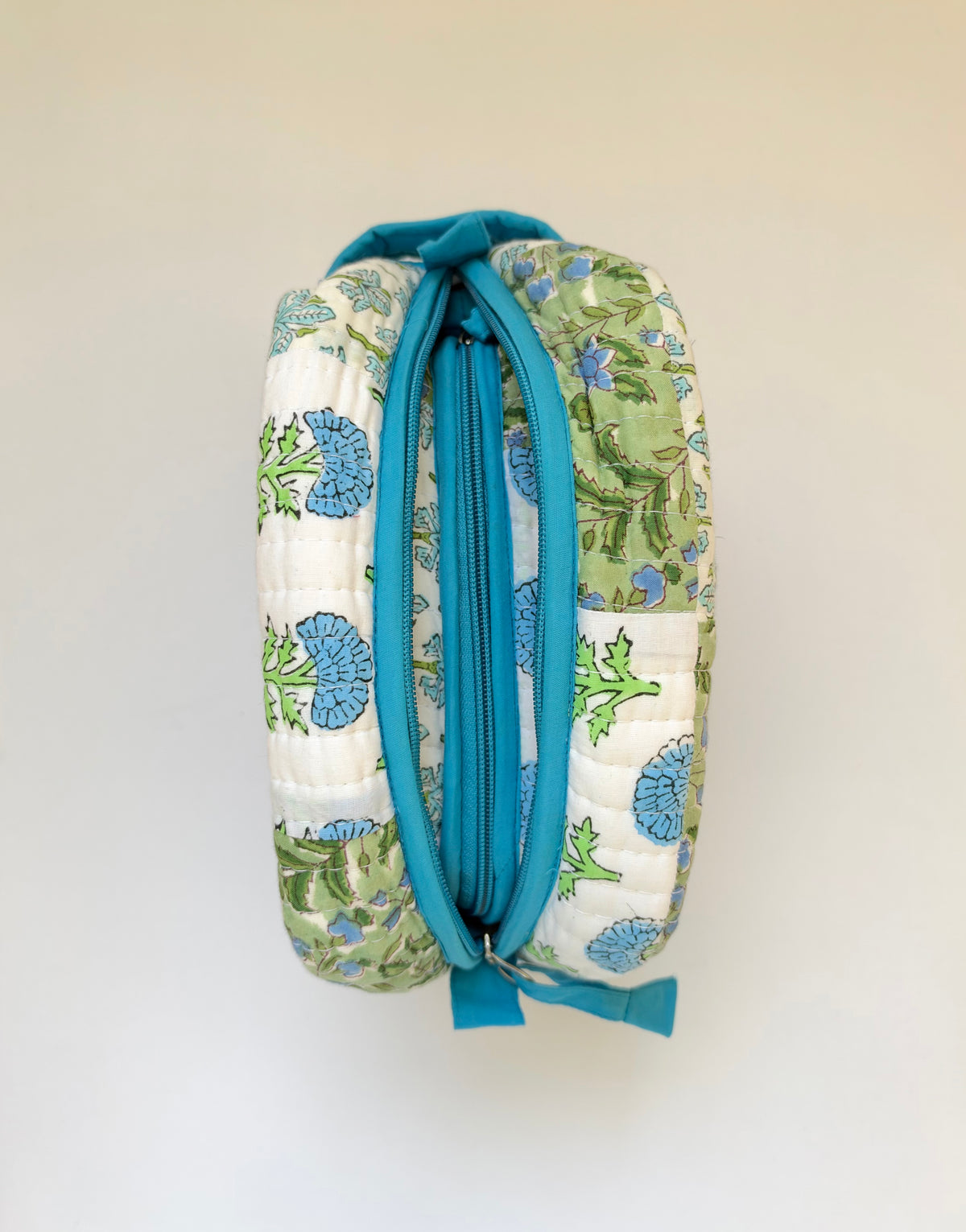 House of Mulmul - Handblock Printed Travel Makeup Quilted Pouch set. A quilted cosmetic pouch with a blue and green floral pattern on a white background, featuring a prominent blue zipper and handle.