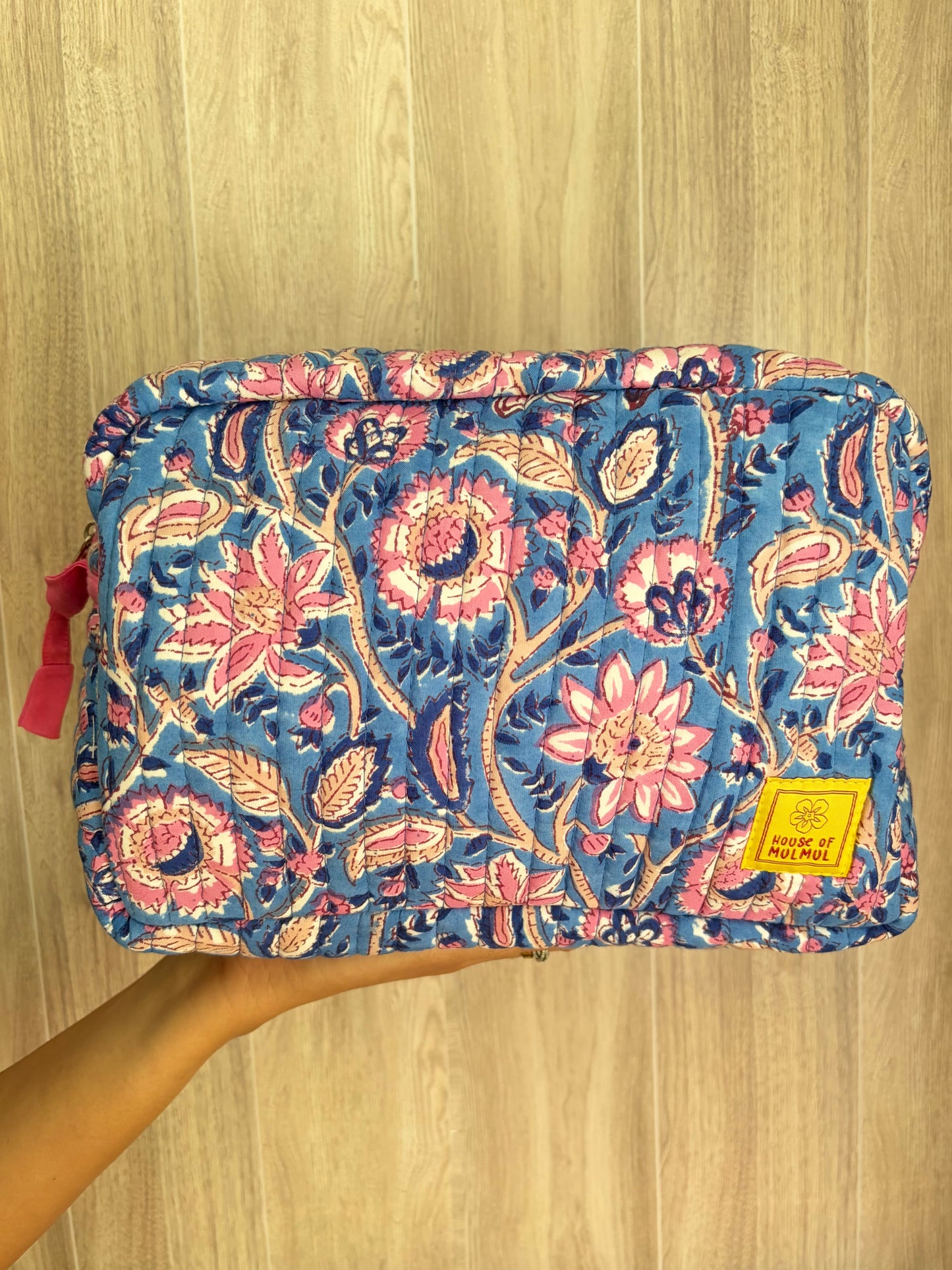 House of Mulmul - Quilted Blockprint Travel Makeup pouch. Blue Pink Floral patterned makeup bag held by a hand on a wooden surface.