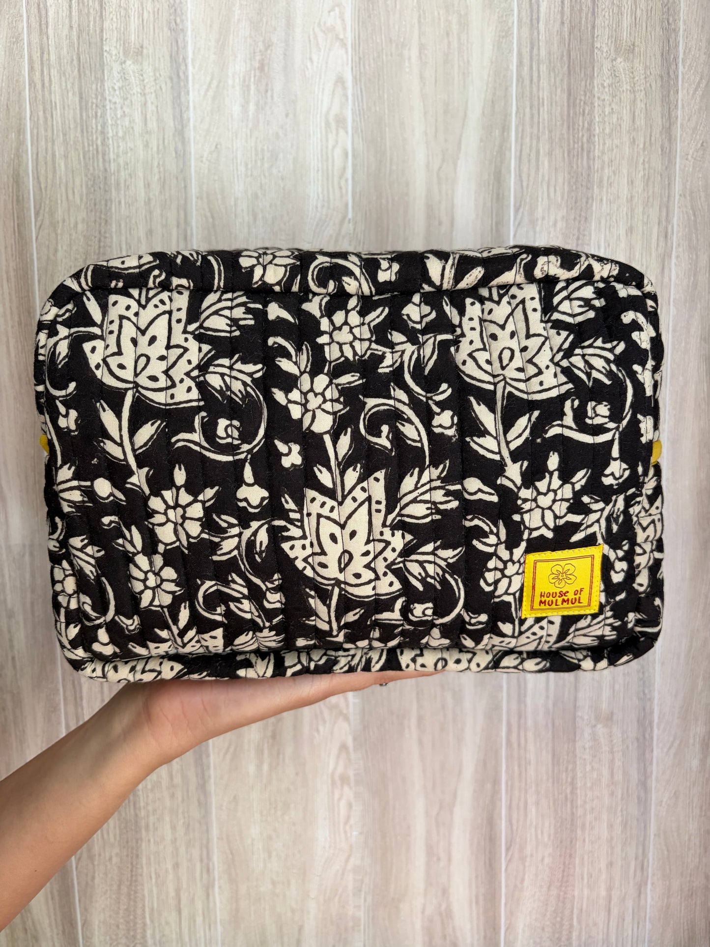 House of Mulmul - Quilted Blockprint Travel Makeup pouch. Black Beige Floral patterned makeup bag held by a hand on a wooden surface.