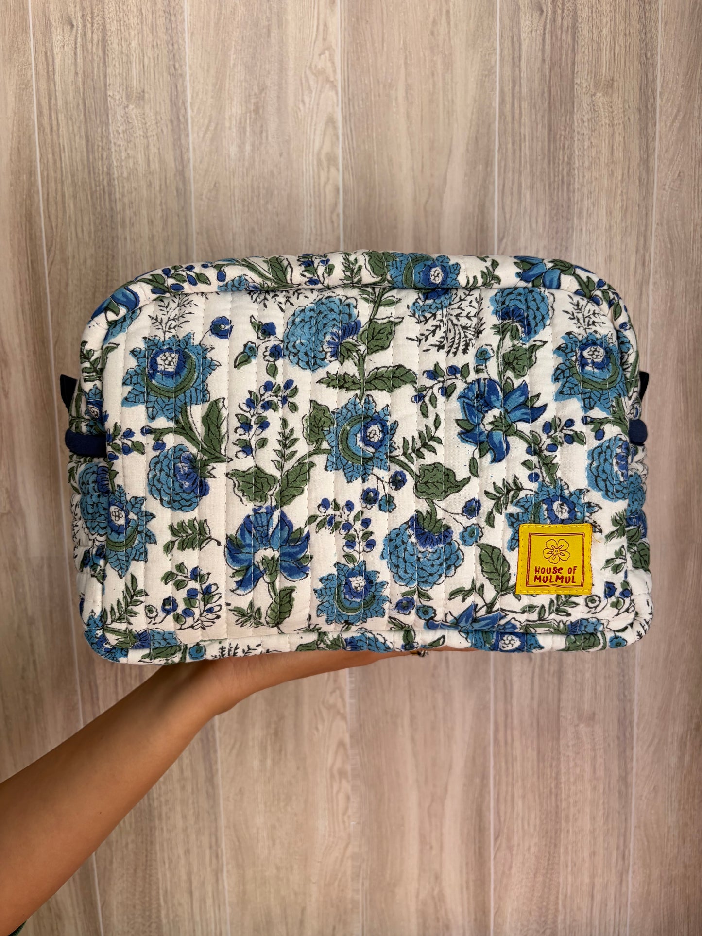 House of Mulmul - Quilted Blockprint Travel Makeup pouch. Blue White Green Floral patterned makeup bag held by a hand on a wooden surface.