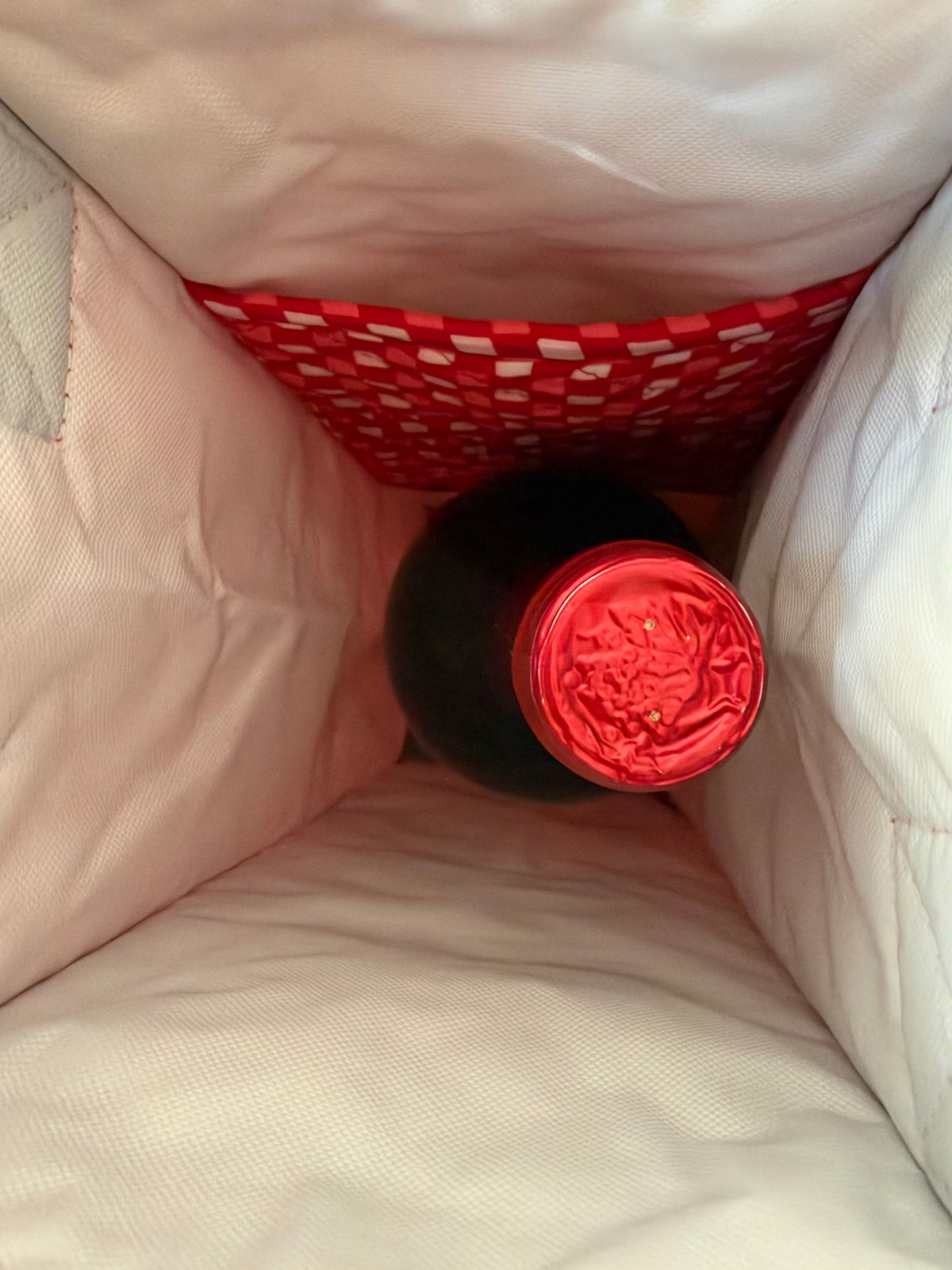 House of Mulmul - Quilted Wine Tote Bag. A close-up view inside a light pink insulated bag or cooler, showing a dark bottle with a bright red cap or foil top resting in a red-and-white checkered pocket.