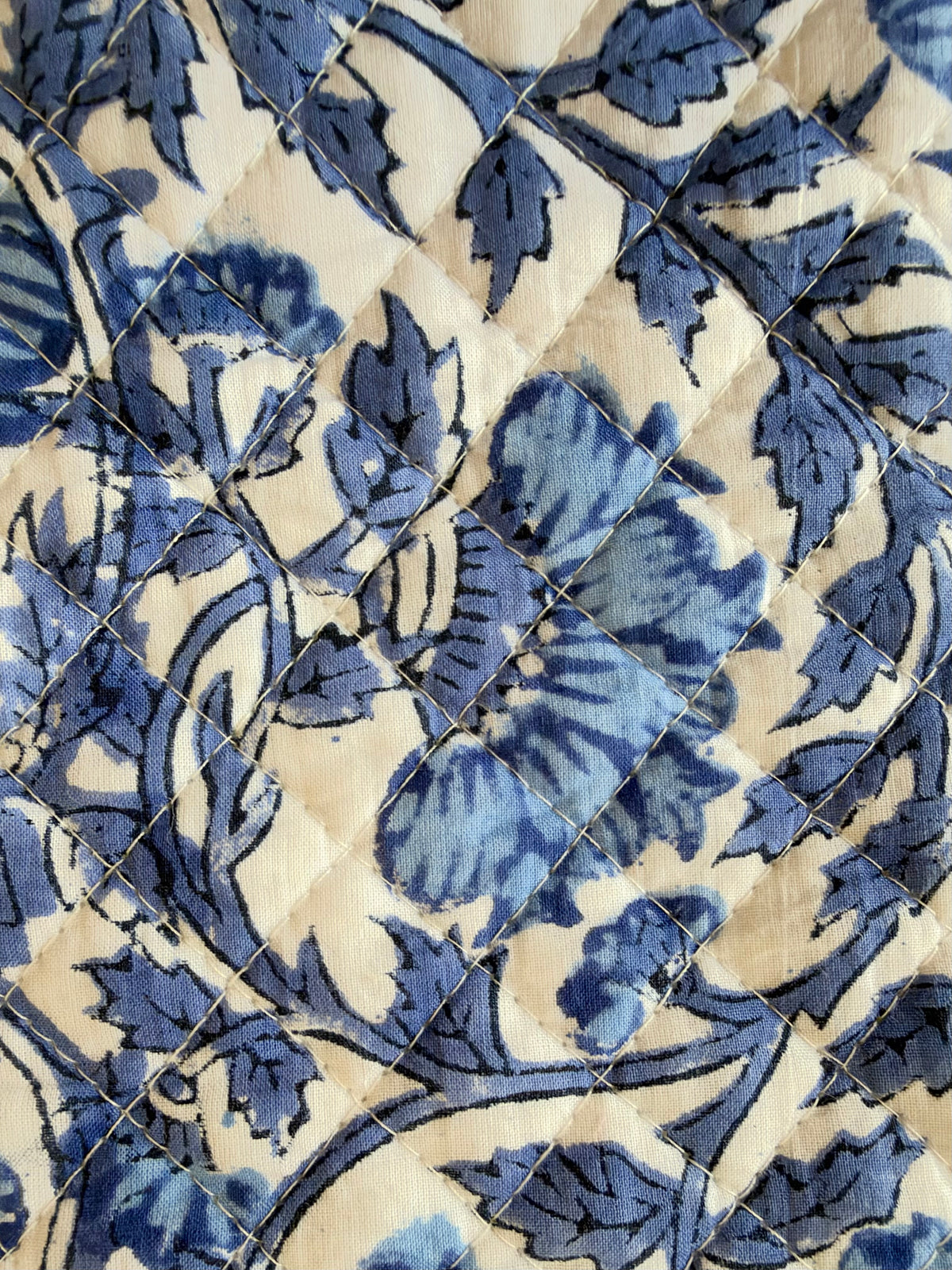 House of Mulmul - Quilted Wine Tote Bag. A close-up of a quilted textile featuring a blue floral and leaf pattern on a warm cream background, arranged in a diamond-quilted design.