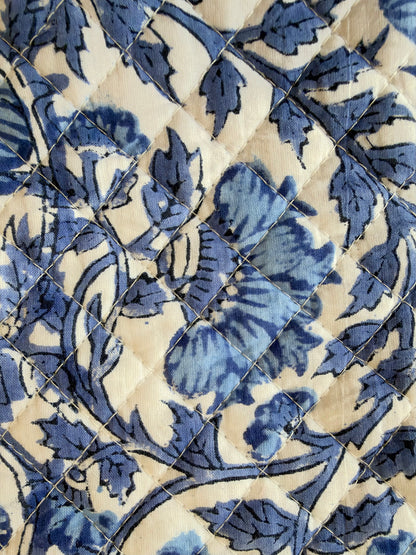 House of Mulmul - Quilted Wine Tote Bag. A close-up of a quilted textile featuring a blue floral and leaf pattern on a warm cream background, arranged in a diamond-quilted design.