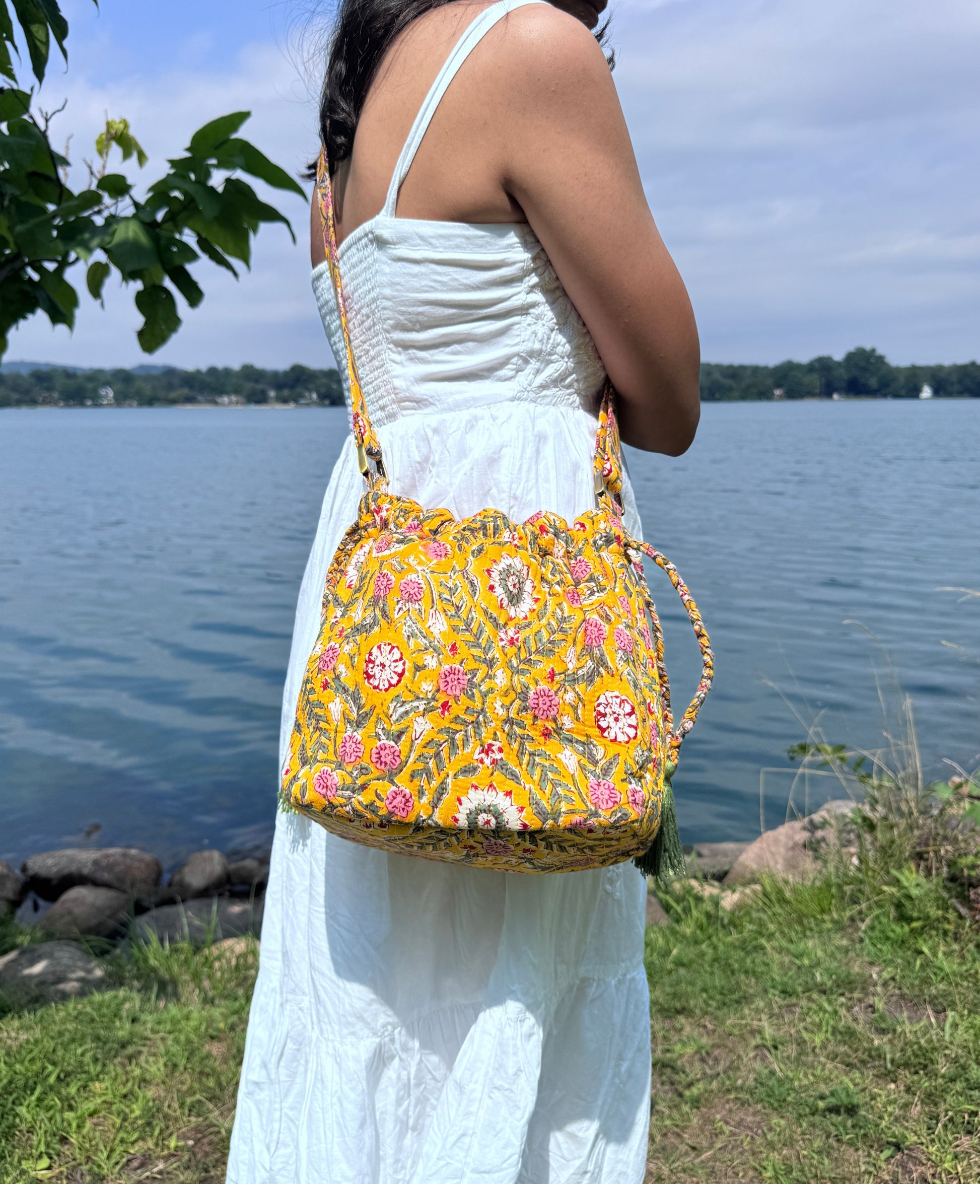 House of Mulmul - Garden Wayfarer Bucket Bag, Cotton bag, Crossbody sling bag. Woman in a white dress holding a yellow floral handbag by a lake