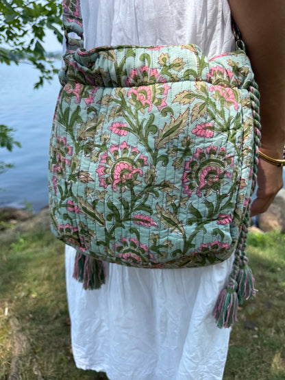 House of Mulmul - Garden Wayfarer Bucket Bag, Cotton bag, Crossbody sling bag. Person holding a floral-patterned bag by a body of water with a decorative border.