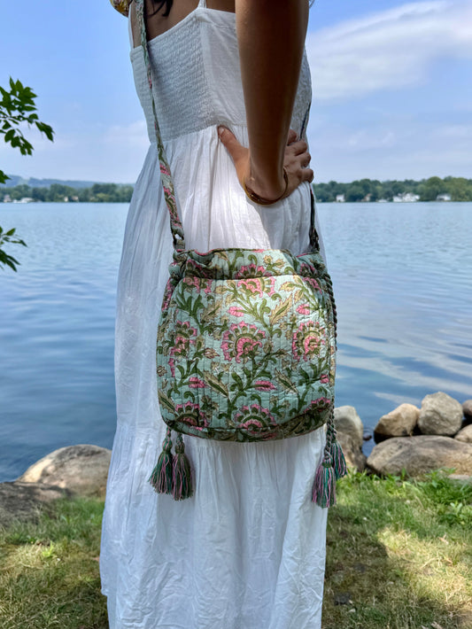 House of Mulmul - Garden Wayfarer Bucket Bag, Cotton bag, Crossbody sling bag. Person holding a floral-patterned bag by a body of water with a decorative border.