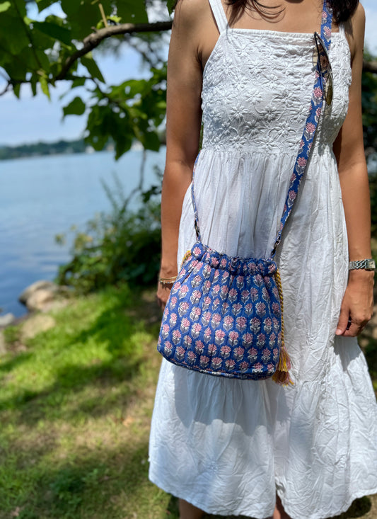 House of Mulmul - Garden Wayfarer Bucket Bag, Cotton bag, Crossbody sling bag. Woman in a white dress with a blue floral bag standing by a body of water.