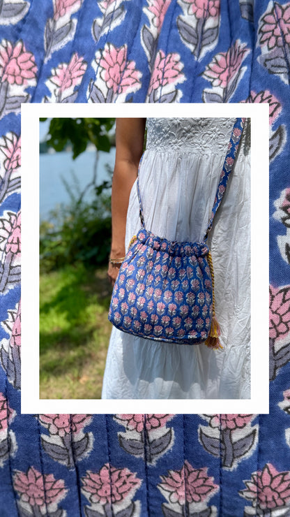 House of Mulmul - Garden Wayfarer Bucket Bag, Cotton bag, Crossbody sling bag. Person wearing a white dress with a blue floral-patterned bag outdoors.