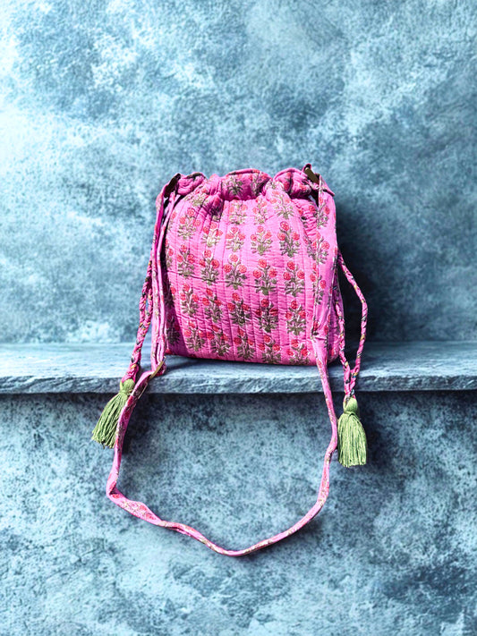 House of Mulmul - Garden Wayfarer Bucket Bag, Cotton bag, Crossbody sling bag. Pink embroidered drawstring bag with tassels on a stone ledge
