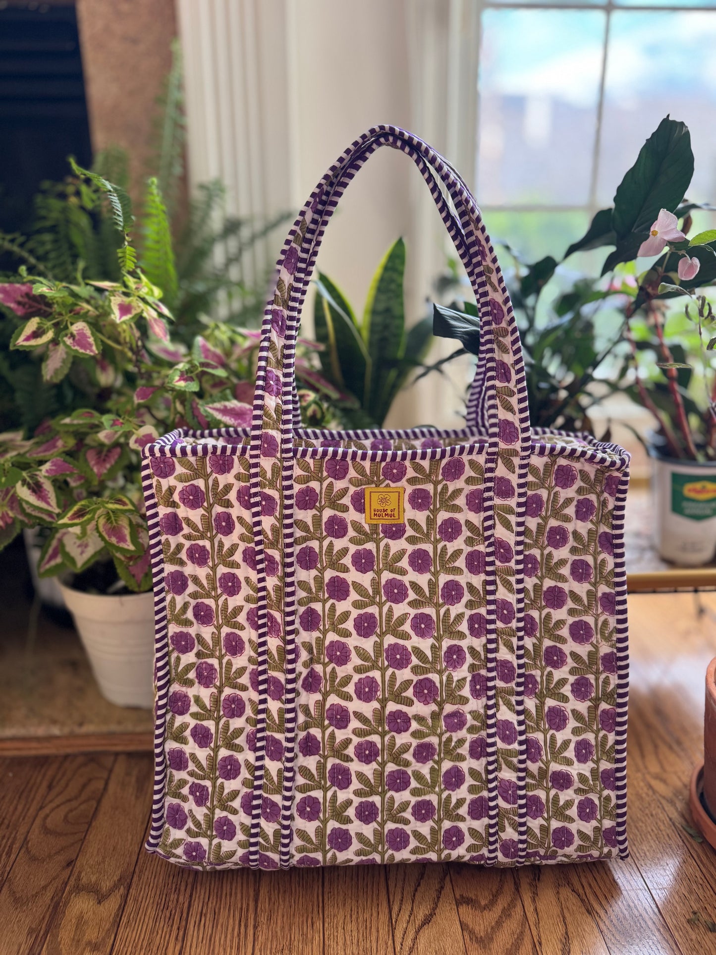 House of Mulmul - Cotton Tote Bag, Travel Bag. Floral-patterned tote bag on a wooden floor with plants in the background