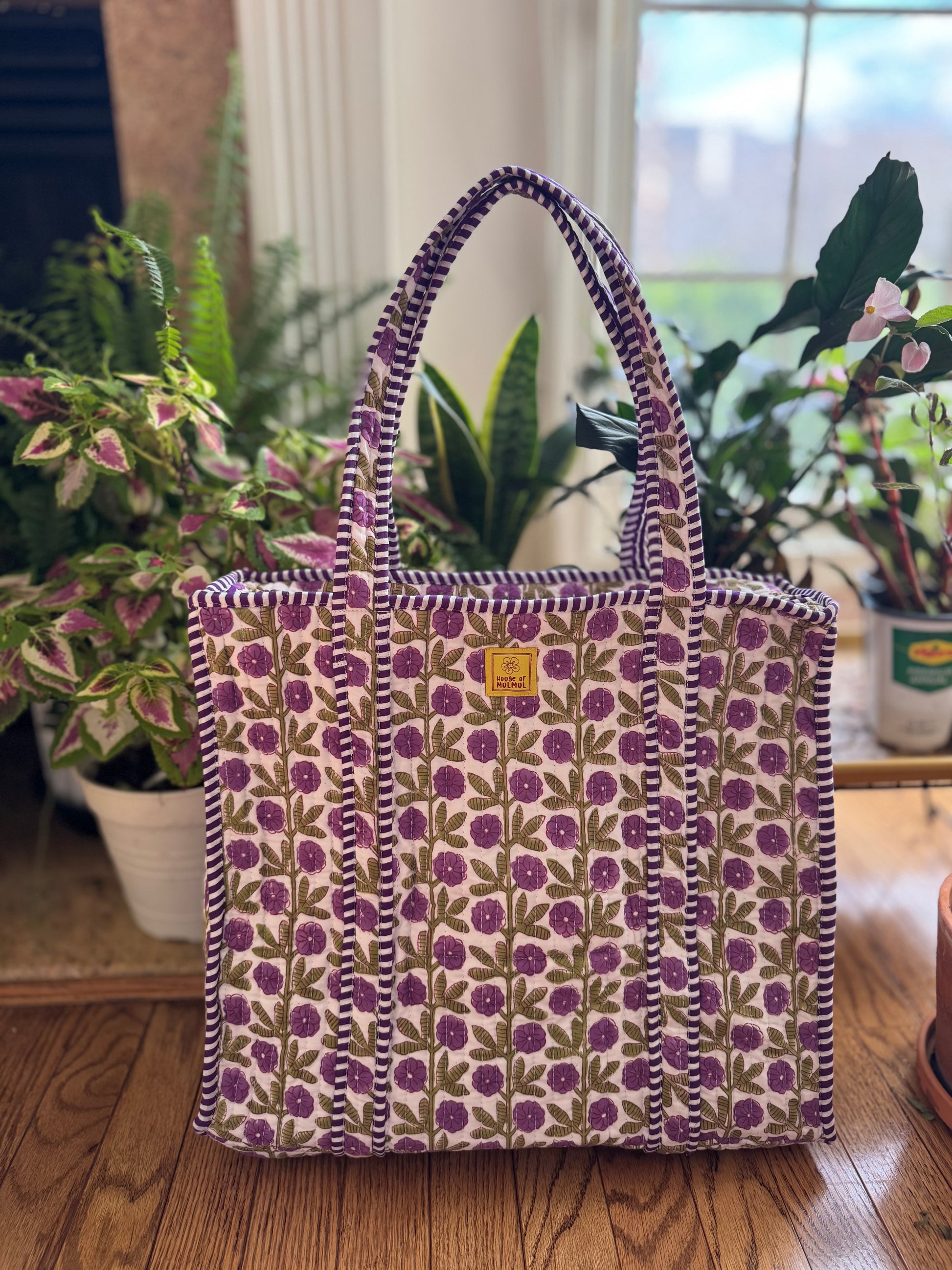 House of Mulmul - Cotton Tote Bag, Travel Bag. Floral-patterned tote bag on a wooden floor with plants in the background