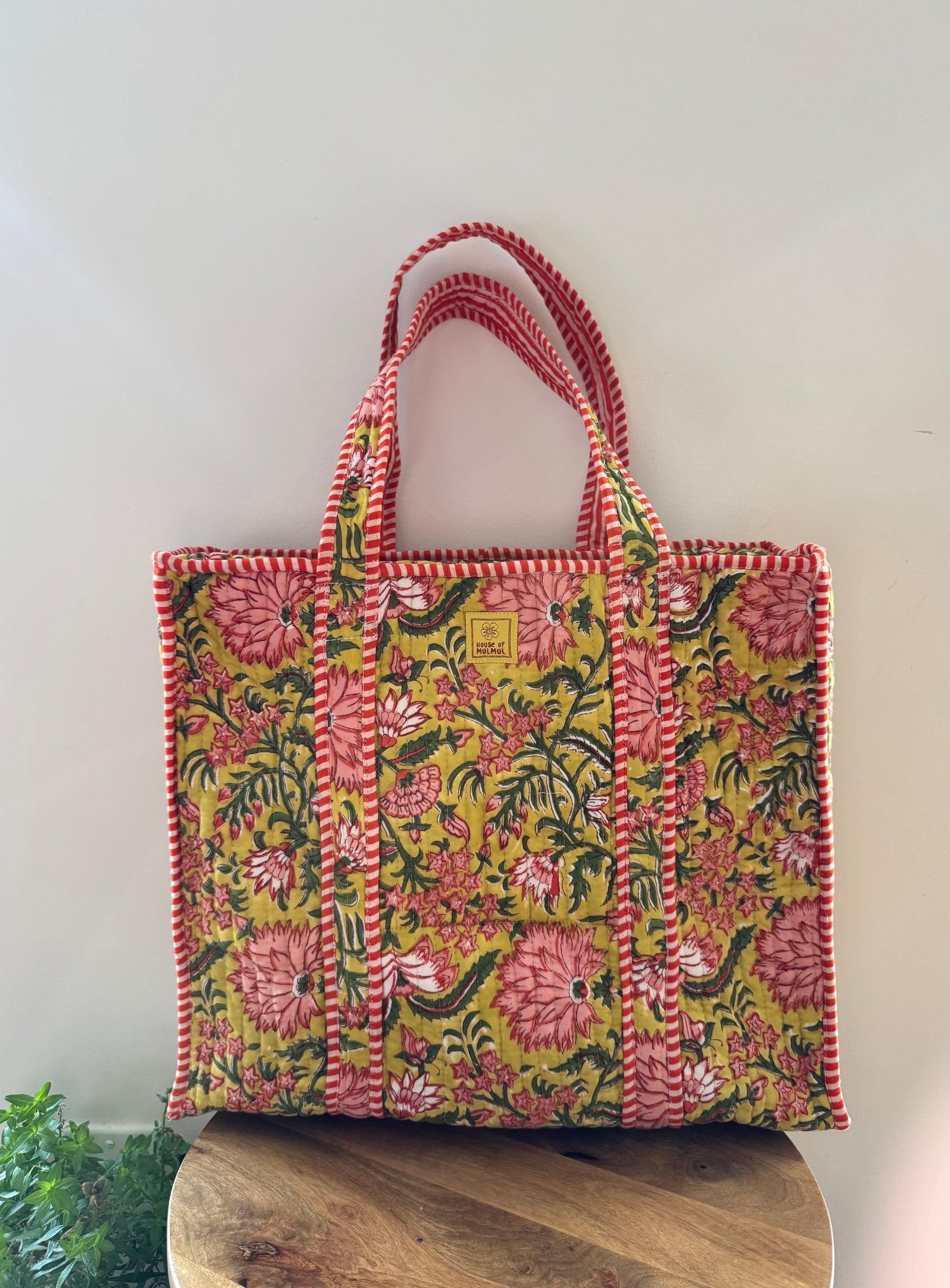 House of Mulmul - Cotton Tote Bag, Travel Bag. Floral patterned tote bag with red accents on a wooden stool against a light background