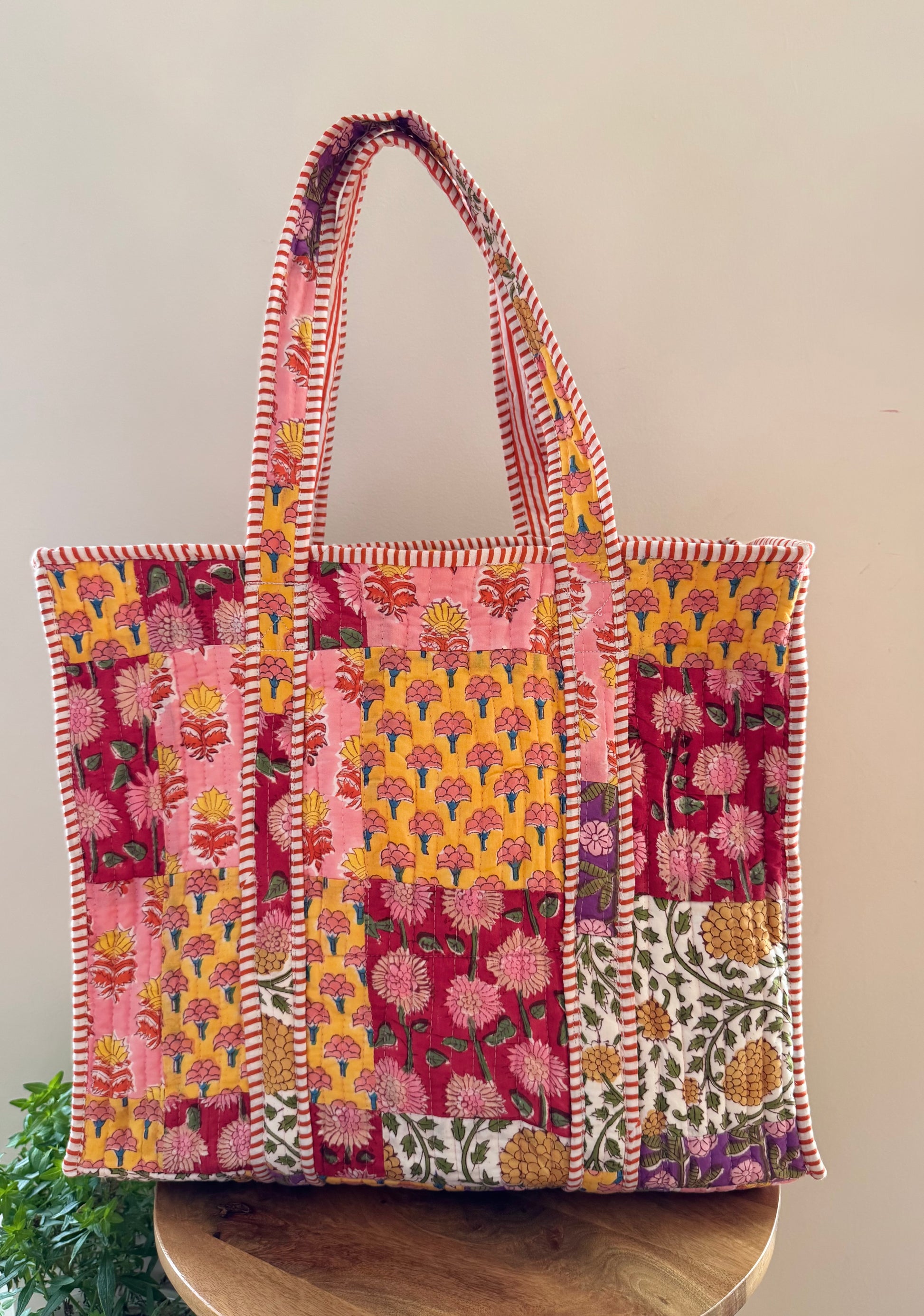 House of Mulmul - Cotton Tote Bag, Travel Bag. Colorful patchwork tote bag with floral patterns on a wooden surface.