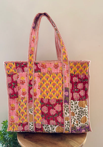 House of Mulmul - Cotton Tote Bag, Travel Bag. Colorful patchwork tote bag with floral patterns on a wooden surface.